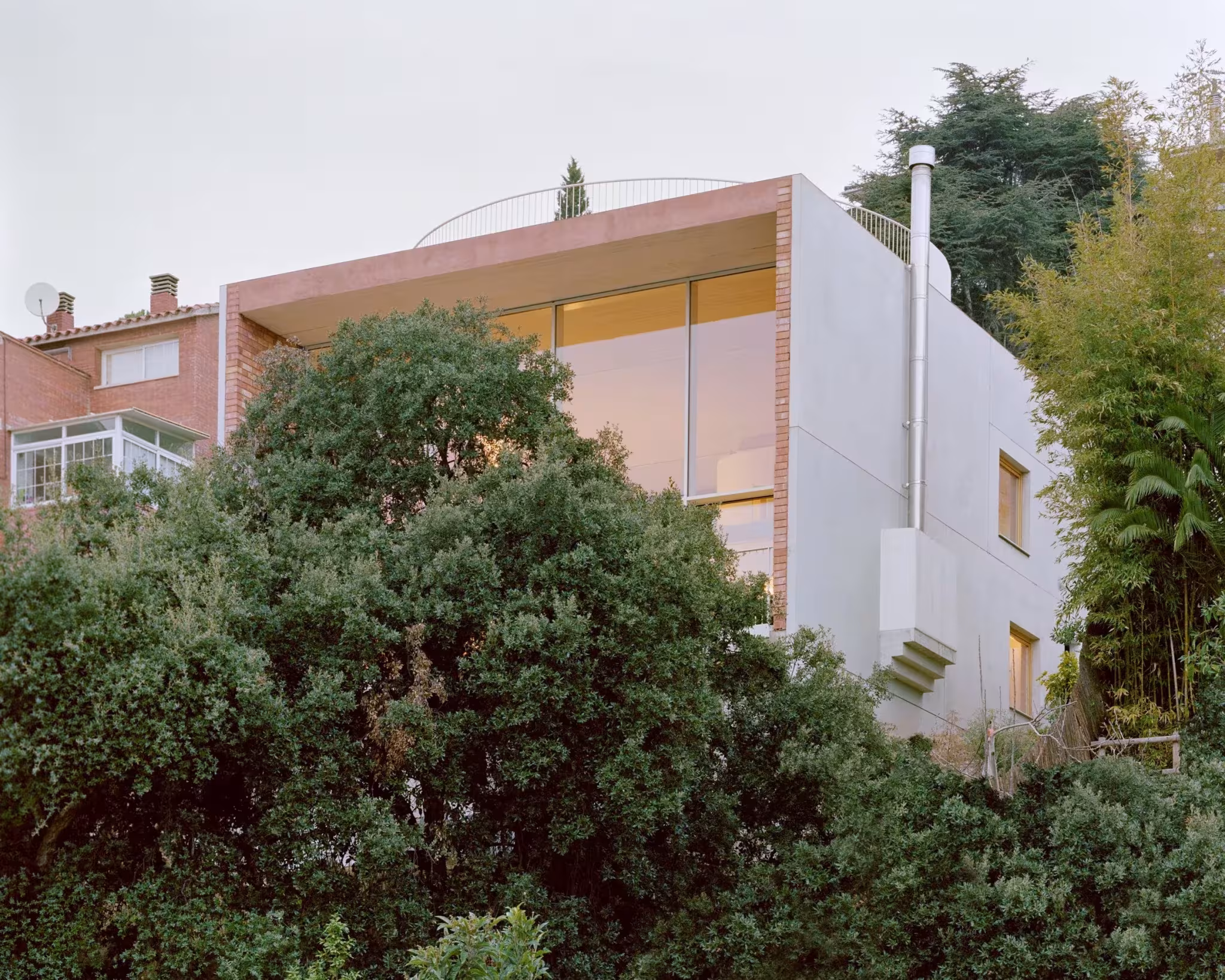Exterior de la Casa Dosmurs de Mesura en Alella, volumen blanco con ventanal asomando entre vegetación densa