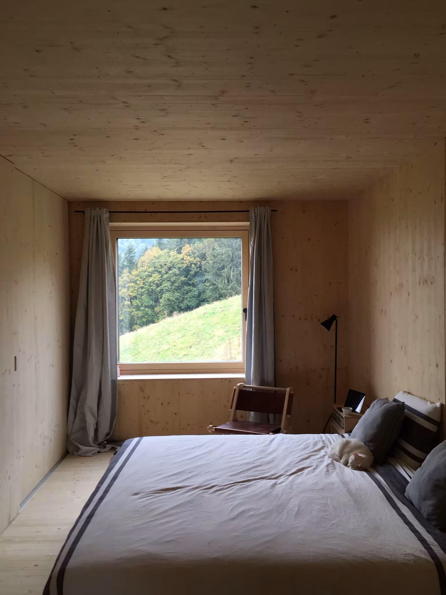 Dormitorio revestido de madera clara con cama y ventana a una ladera verde en el proyecto de LVPH