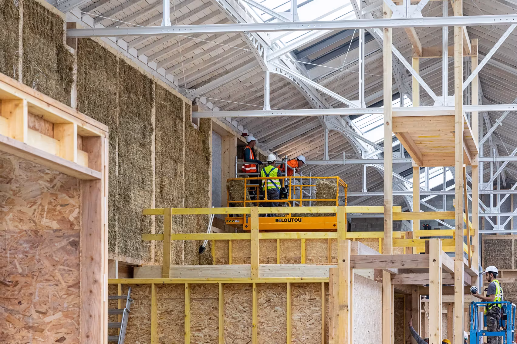 Obra del muro de paja y estructura de madera en la nave de Le Magasin Électrique, con operarios en plataforma