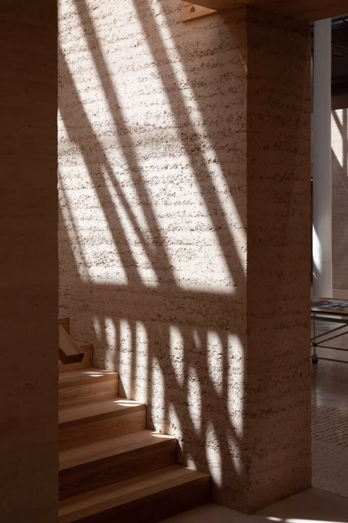 Escalera de madera junto a un muro de tierra con sombras de luz en Le Magasin Électrique