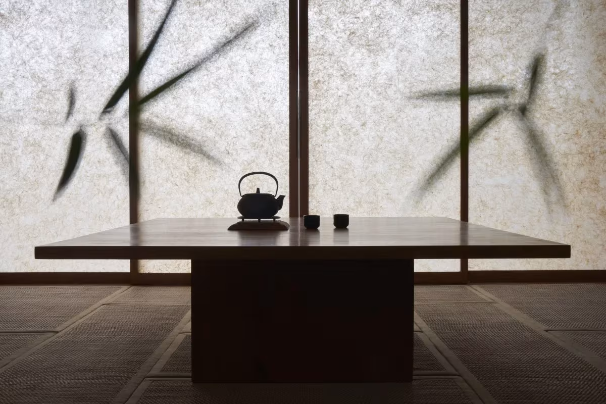 Mesa baja de madera ante paneles translúcidos con sombras de bambú en HER