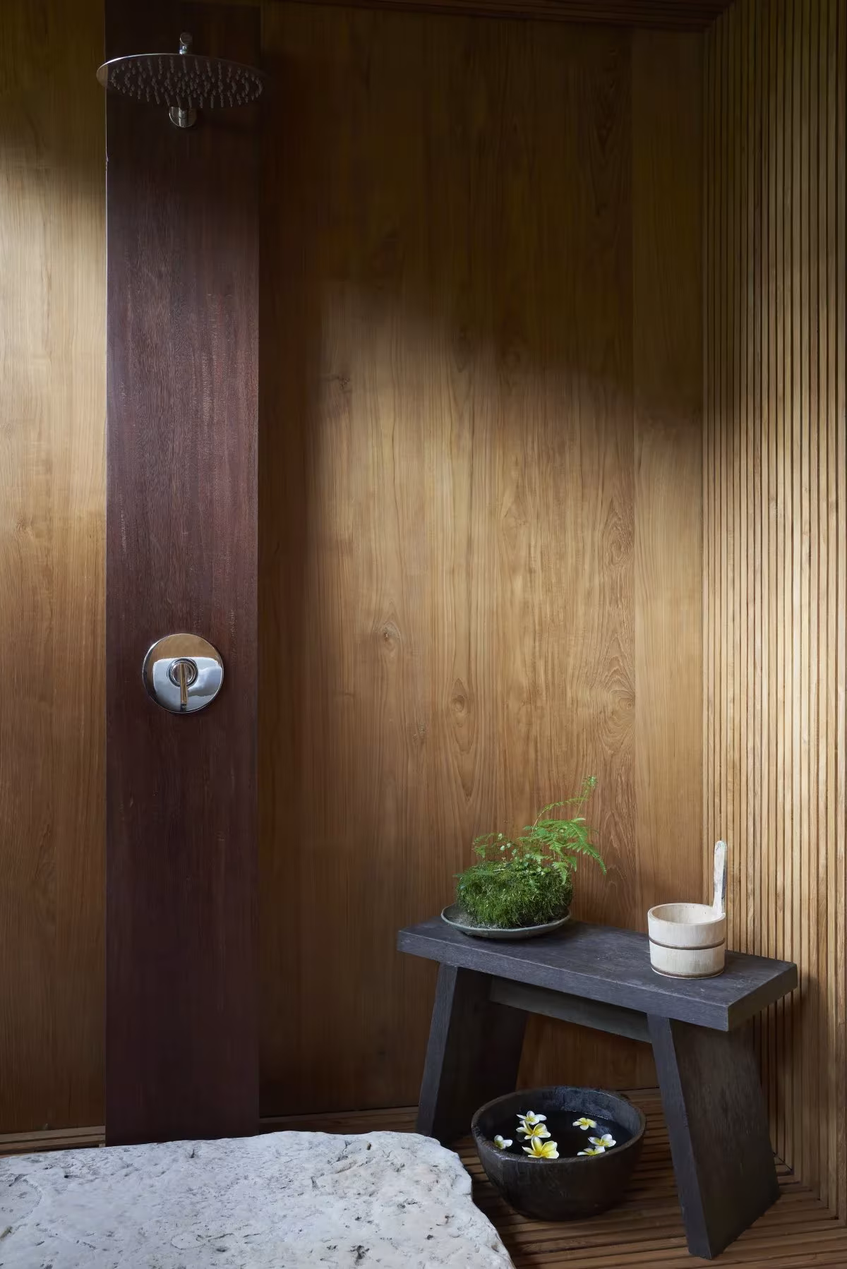 Ducha exterior con taburete de madera y revestimiento de listones en el refugio HER