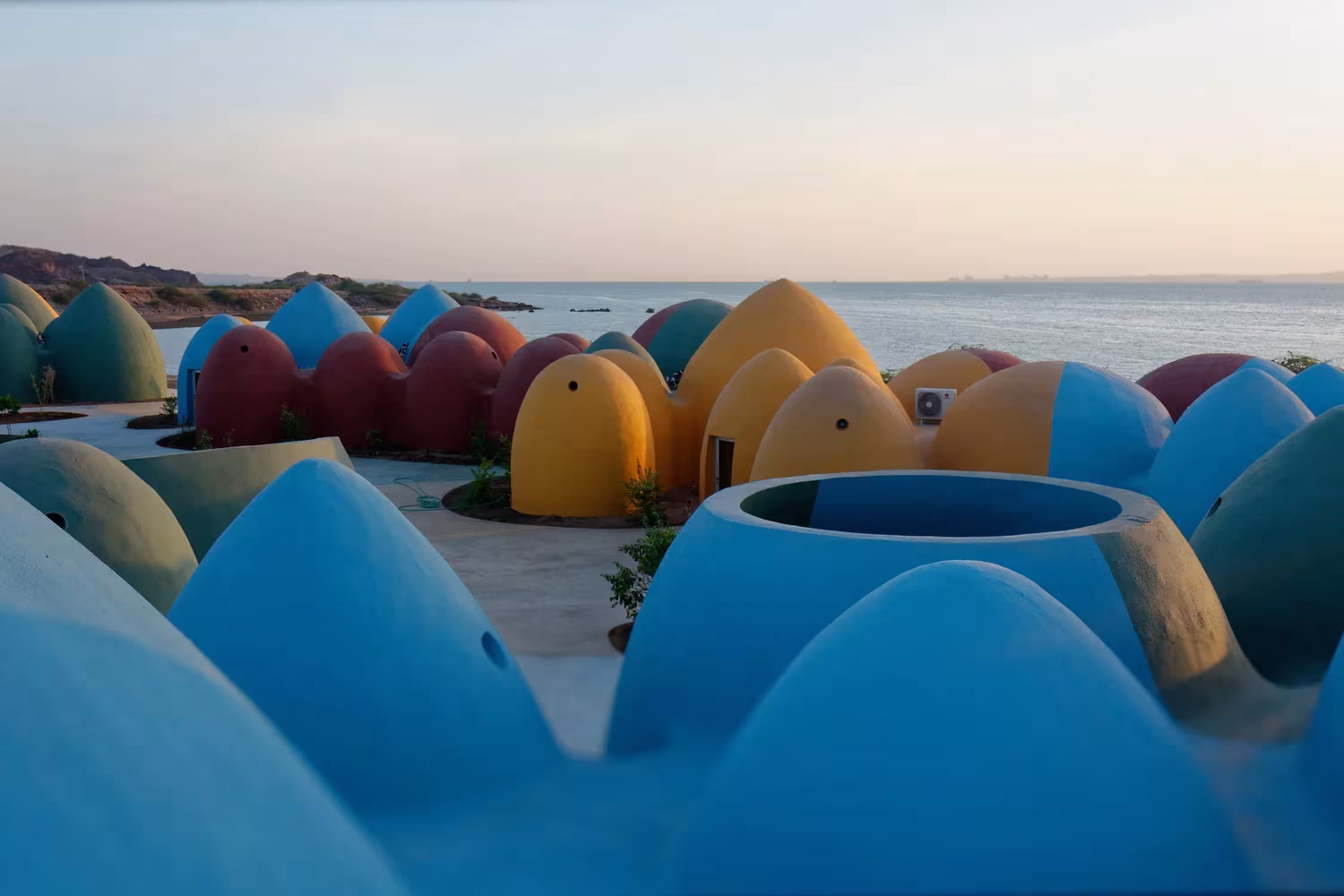 Cúpulas de adobe azules, rojas y amarillas junto al mar al atardecer en el proyecto de ZAV Architects en Ormuz