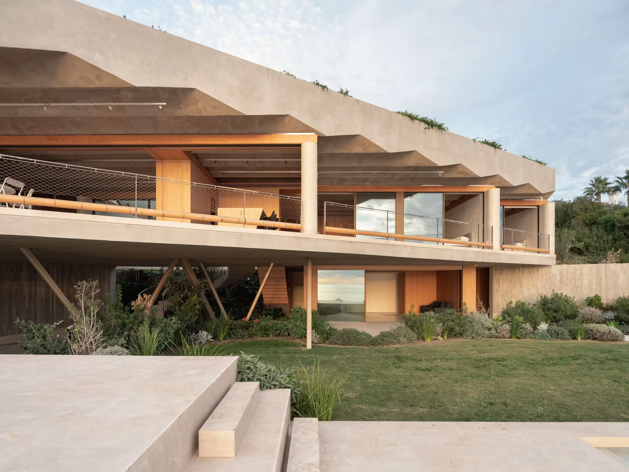 Fachada de madera y vidrio bajo la cubierta plegada de hormigón, con césped delante, en el refugio de Langarita Navarro