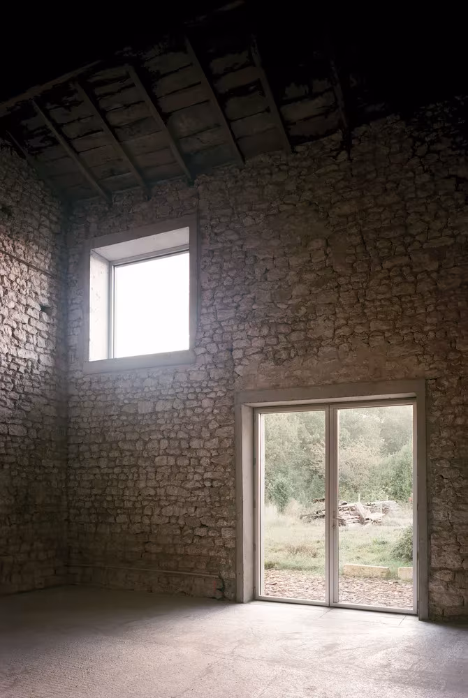 Muro interior de piedra con dos aberturas en el granero convertido en casa por Migeon Architecture