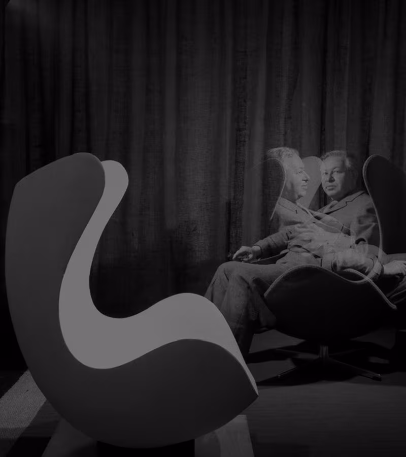 Egg chair in black and grey beside a black and white portrait of Arne Jacobsen seated in one