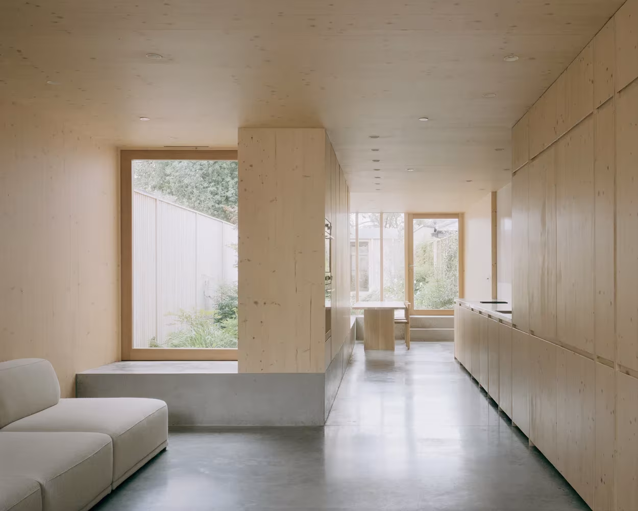 Interior de la Casa y estudio Spruce con sofá gris, suelo de hormigón y armarios de madera a lo largo del muro