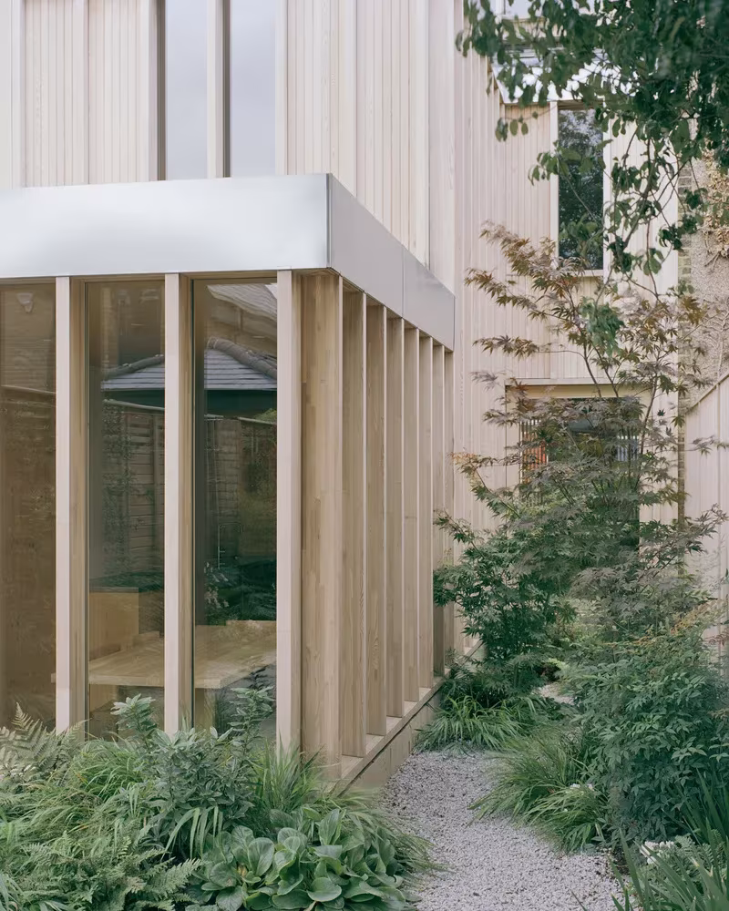 Volumen acristalado con pilares de madera en el jardín de la Casa y estudio Spruce, entre helechos y grava