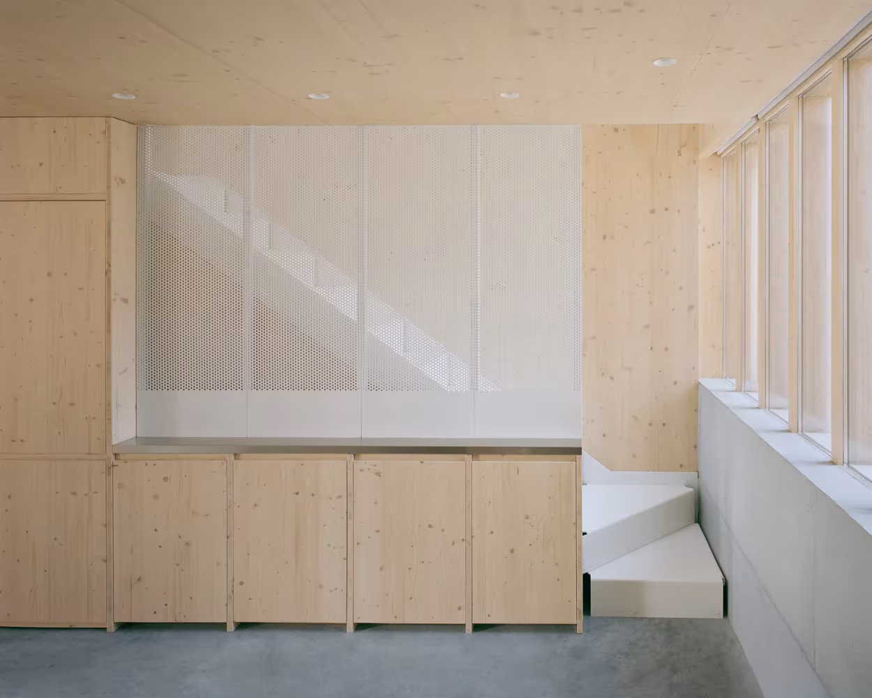 Cocina de la Casa y estudio Spruce con muebles de madera clara, escalera tras panel translúcido y lamas verticales