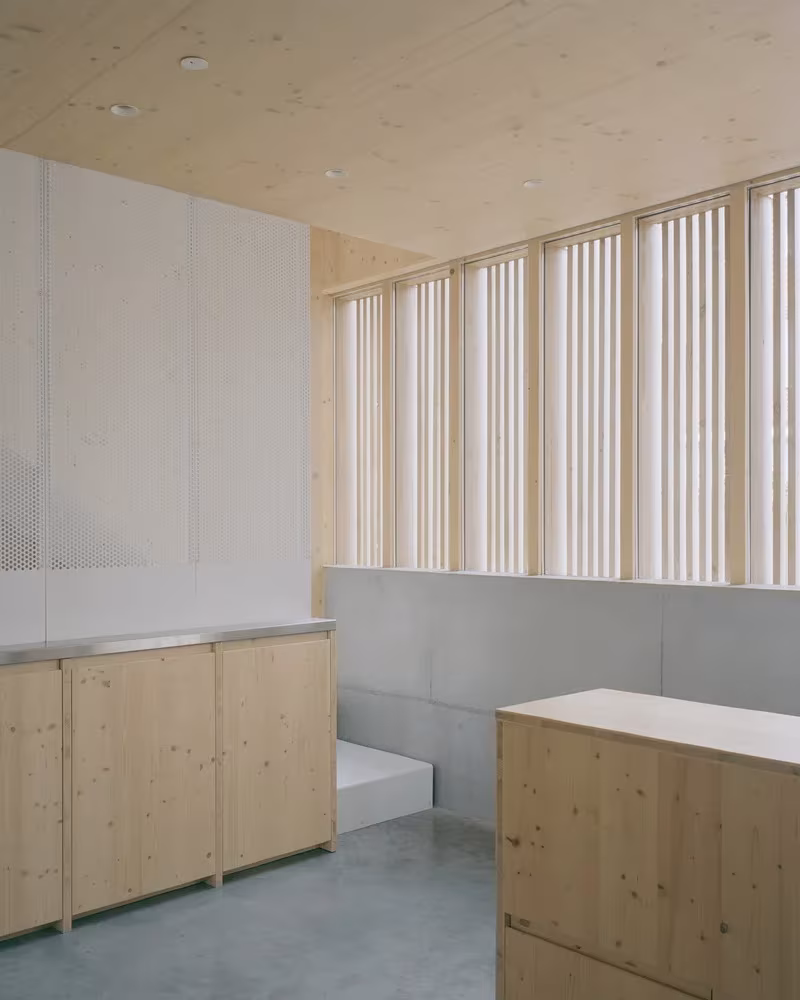 Isla de madera y encimera metálica en la Casa y estudio Spruce, iluminadas por ventanas con lamas
