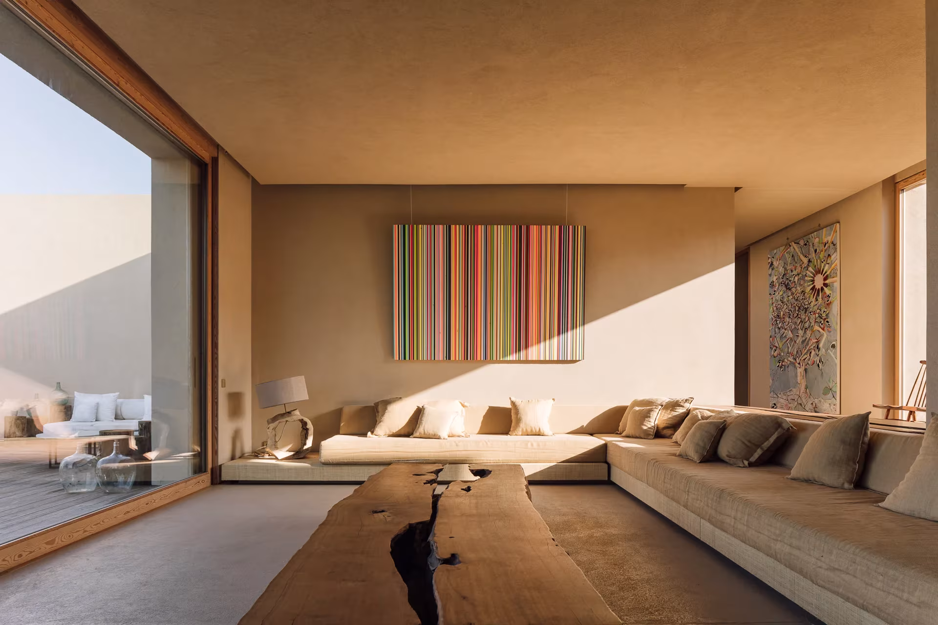 Salón de Melides Art con sofá corrido, mesa de tronco y obras de arte colgadas en muros claros