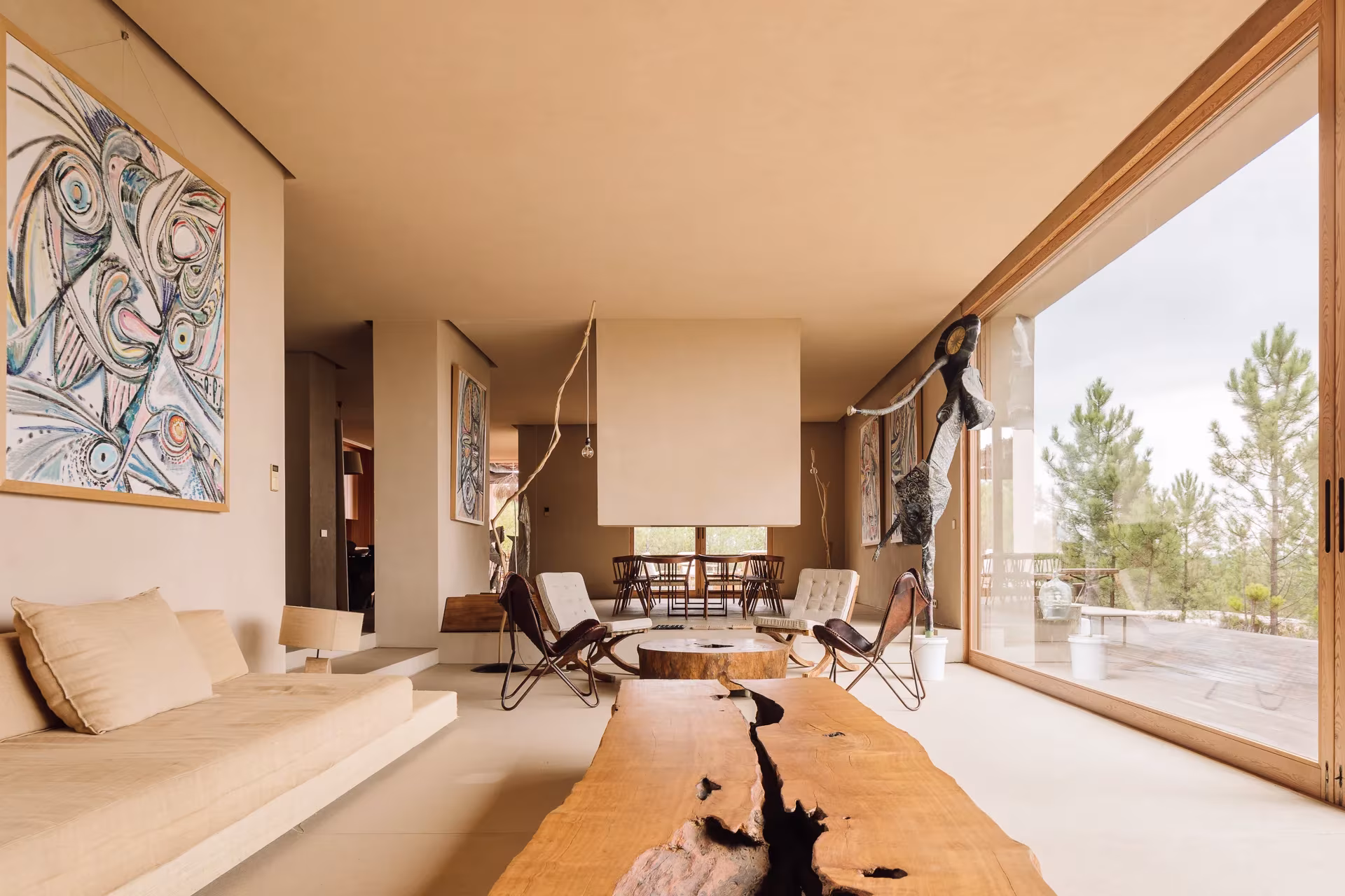 Sala de estar de Melides Art con grandes ventanales al pinar, sillas mariposa y esculturas