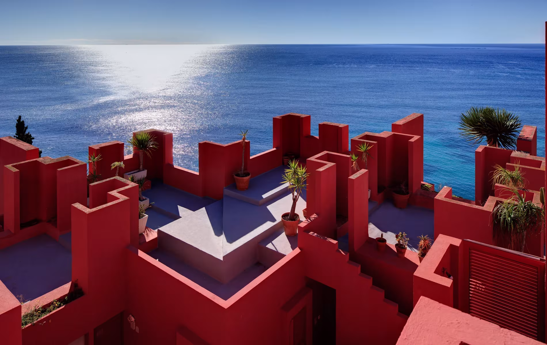Terrazas y almenas rojas de La Muralla Roja de Ricardo Bofill frente al mar Mediterráneo brillante