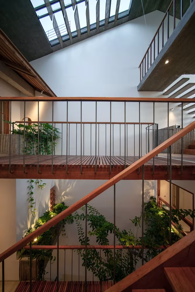 Escaleras y pasarelas de madera con barandillas finas y plantas bajo un lucernario en la Casa Hien