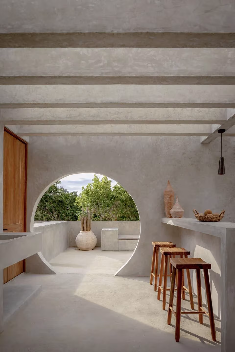Interior de hormigón de Villa Cava con hueco circular al jardín, barra curva y taburetes de madera