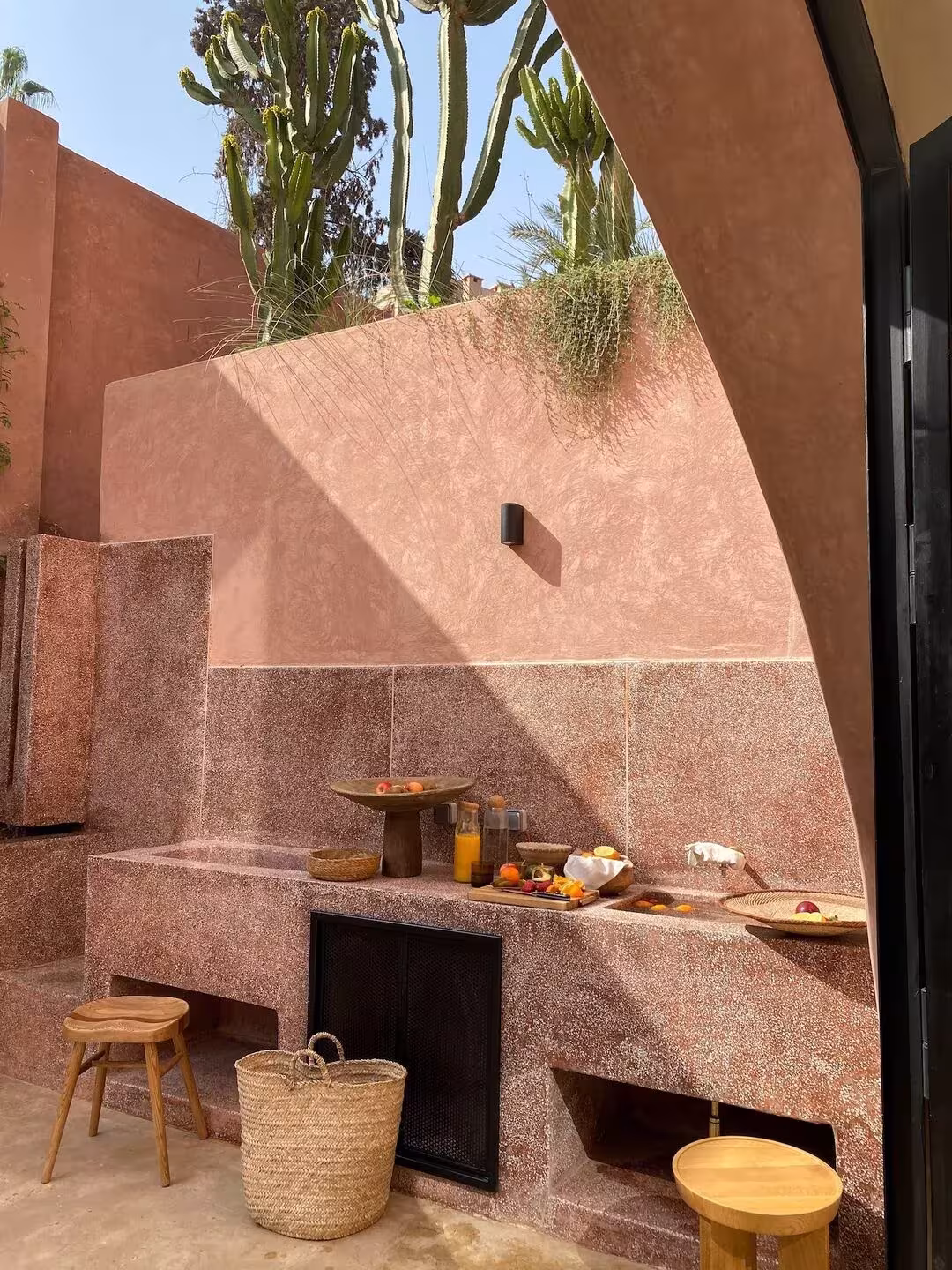 Cocina exterior de Maison Brummell Majorelle con muros rosados, banco de obra, cestos y cactus