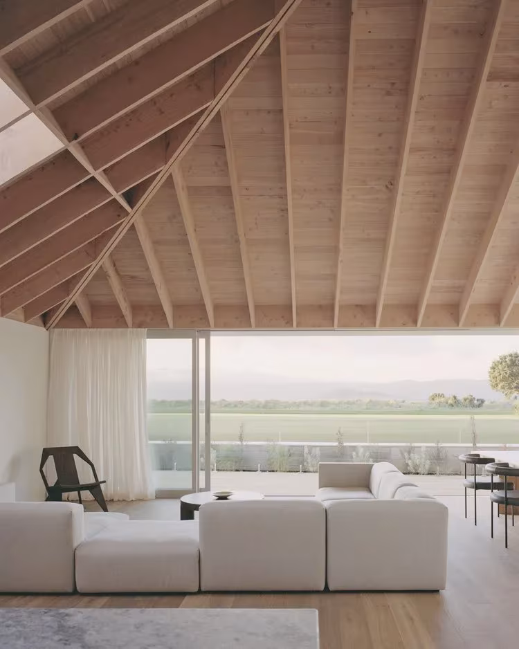 Salón de la RK Residence con techo inclinado de vigas de madera, sofá blanco y ventanal al paisaje