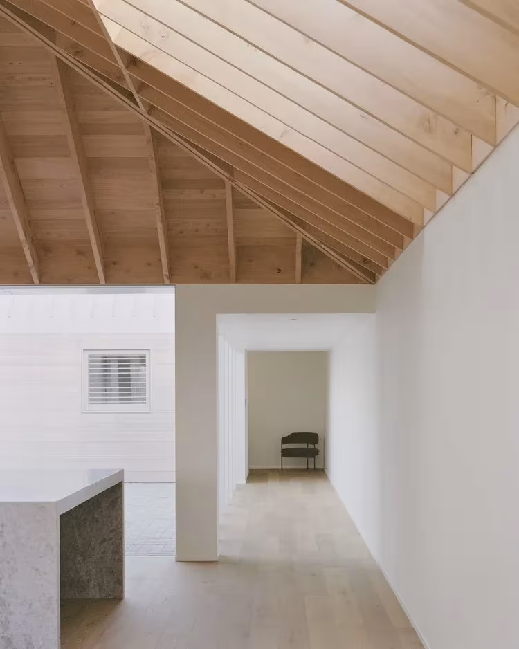 Paso interior de la RK Residence bajo cubierta de madera, con muros blancos y encimera de piedra