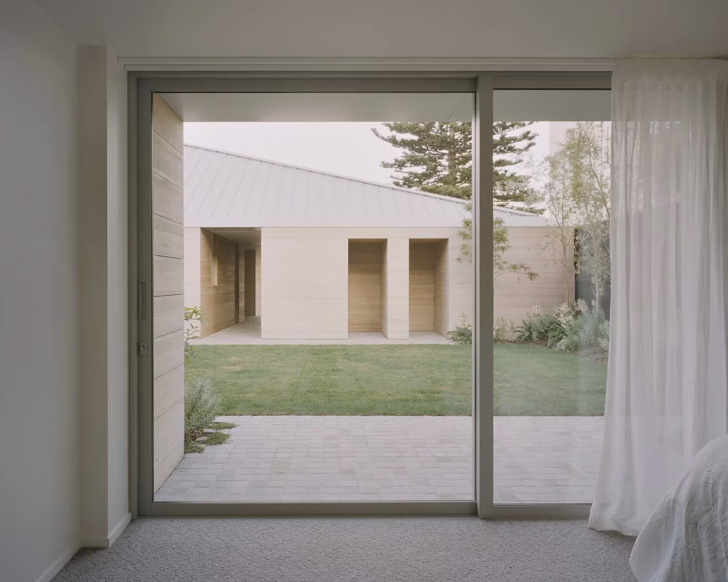 Puerta corredera de la RK Residence con cortina blanca que se abre a un patio de césped