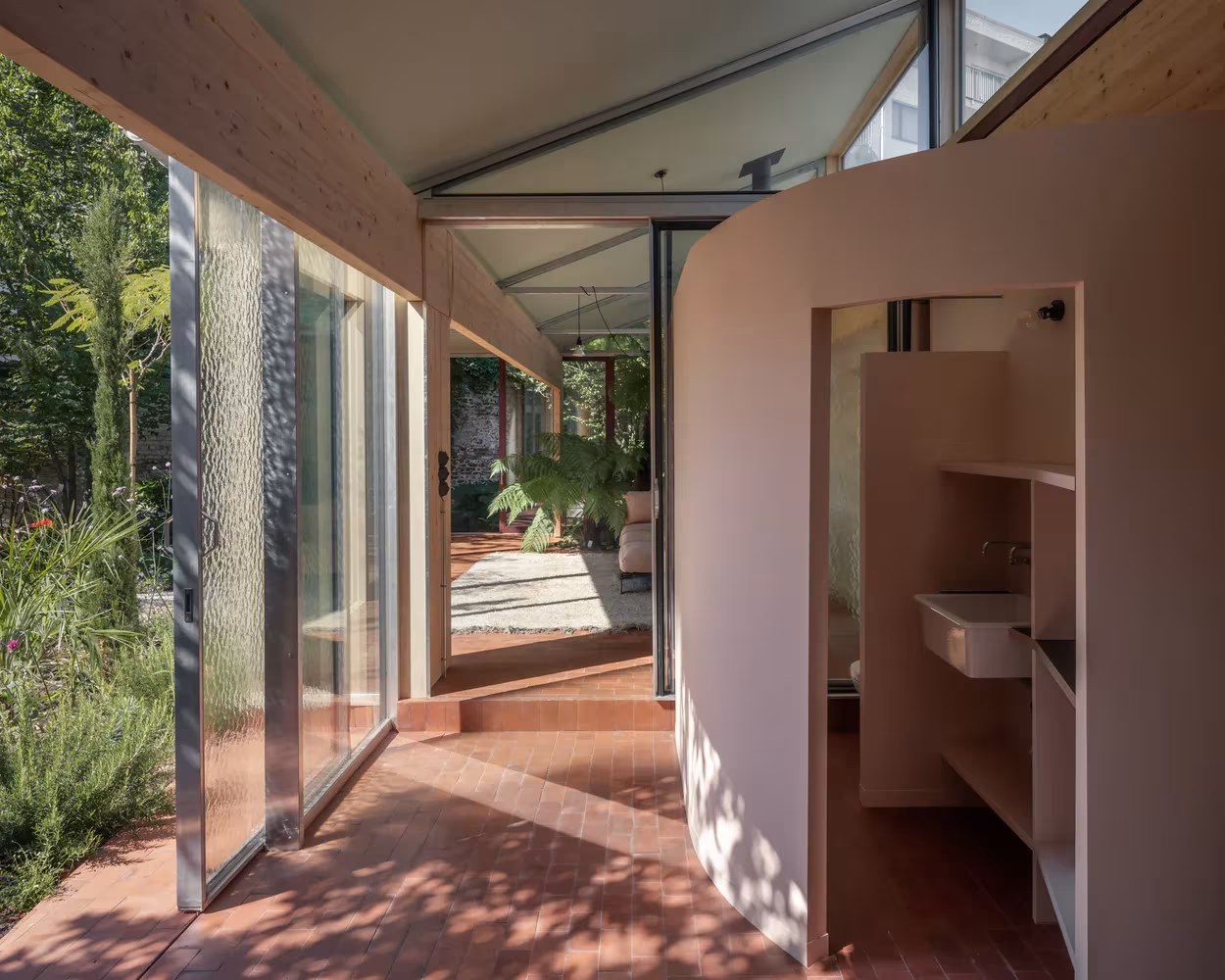 Pasillo acristalado de Martelaar House junto a un volumen curvo rosado que aloja el baño