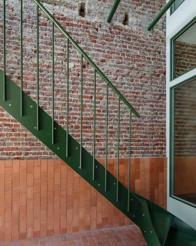 Escalera verde de barandilla metálica junto a un muro de ladrillo visto en Martelaar House