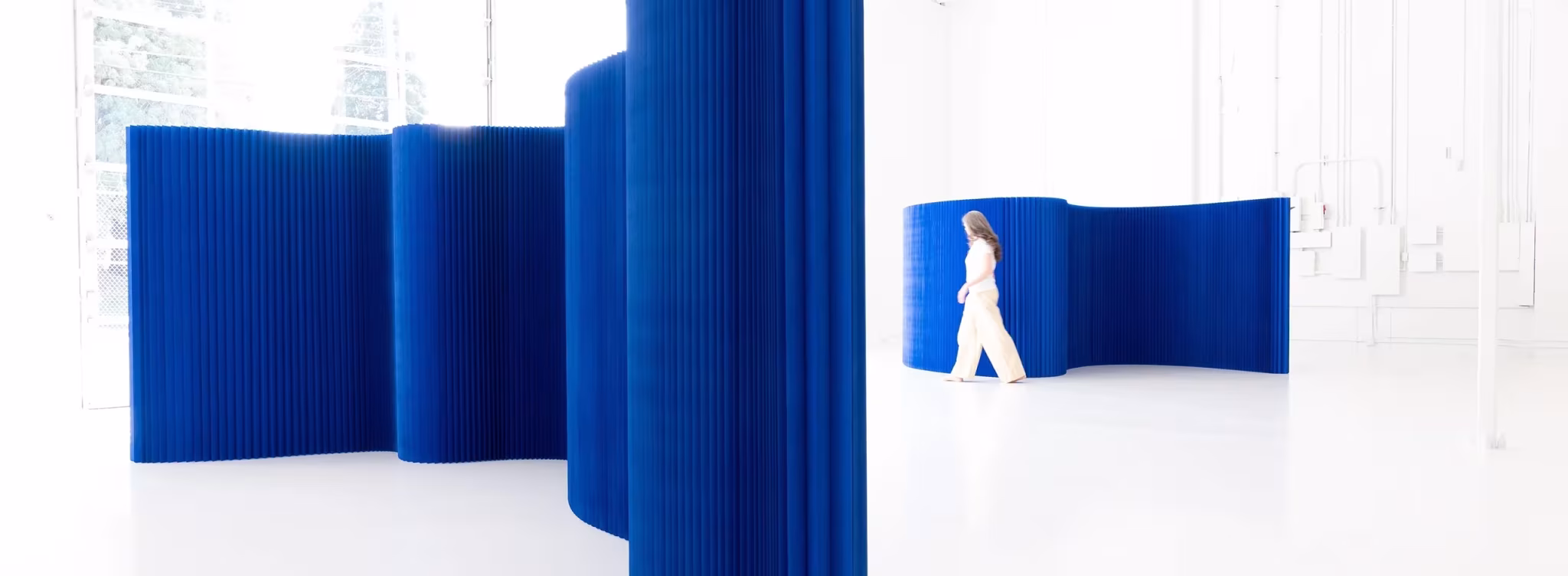 Tabiques plegables de papel azul índigo de molo formando una pared ondulada en un espacio blanco