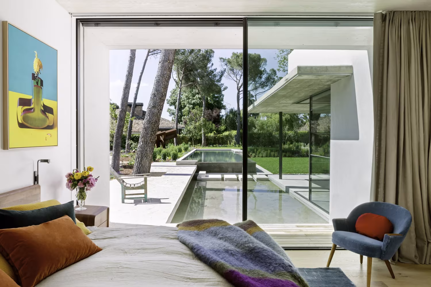 Dormitorio del Proyecto AS de ÁBATON con ventanal a una piscina entre pinos y cuadro de colores