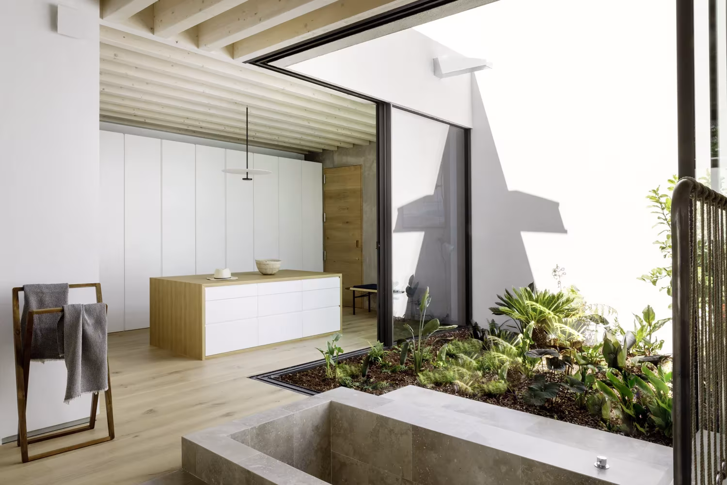 Baño del Proyecto AS de ÁBATON con bañera de piedra junto a un patio de helechos y armarios blancos