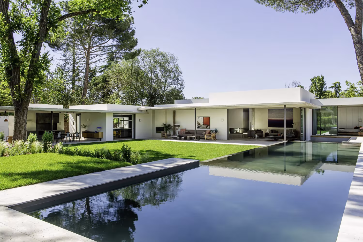 Casa baja del Proyecto AS de ÁBATON en forma de U alrededor de una piscina y césped entre árboles