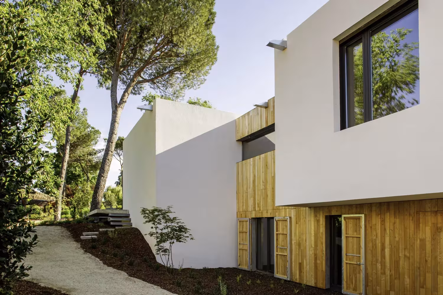 Volúmenes blancos y revestimiento de madera del Proyecto AS de ÁBATON sobre un terreno con pinos