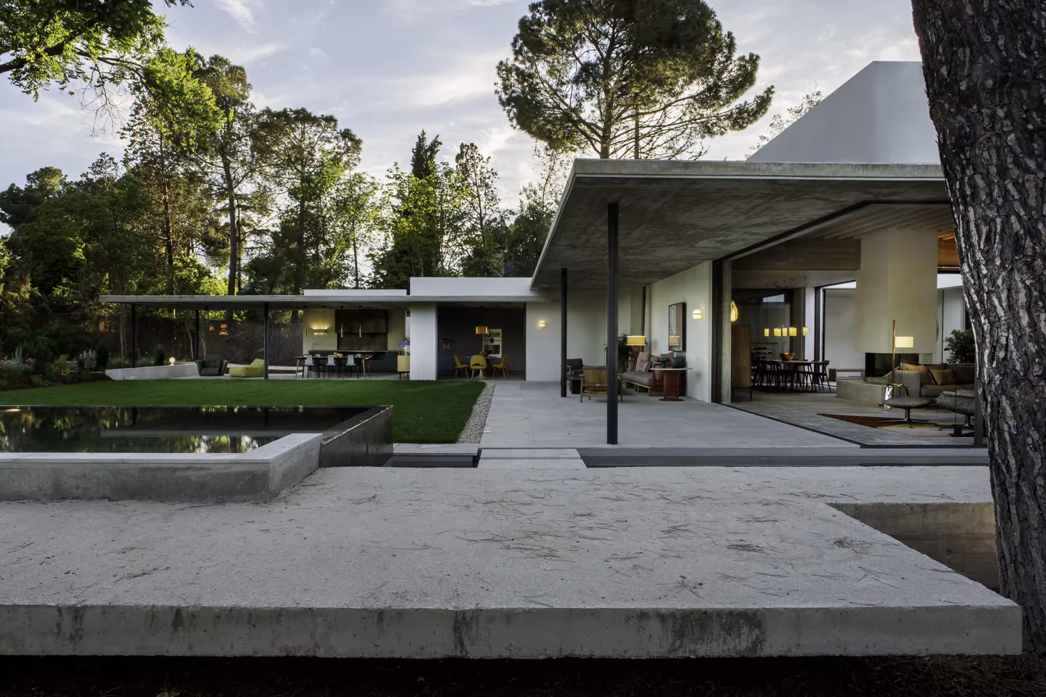 Terraza de piedra del Proyecto AS con lámina de agua y porche de hormigón abierto al jardín