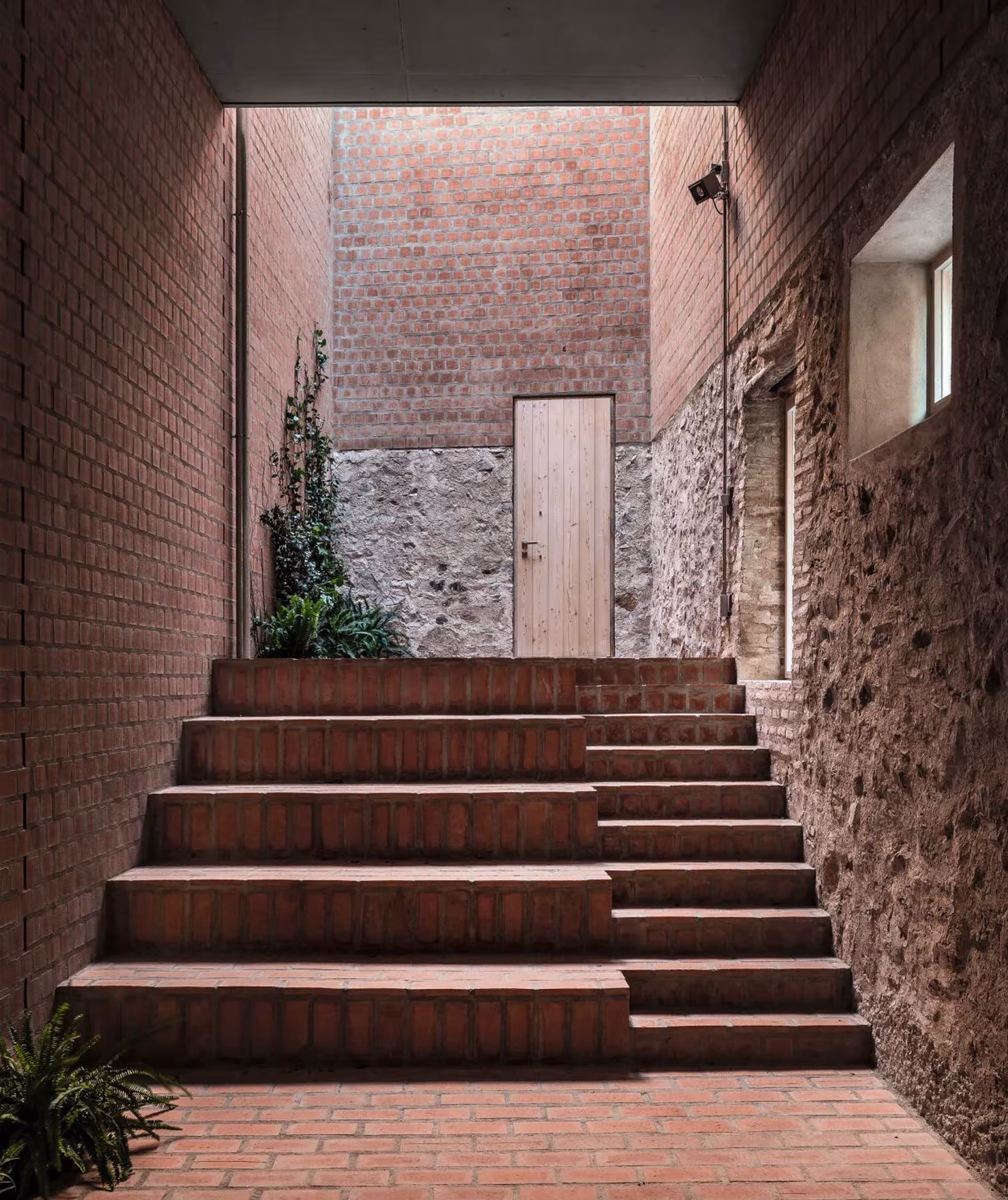 Escalinata de ladrillo en un patio estrecho de las Bodegas Clos Pachem entre muros de piedra y ladrillo