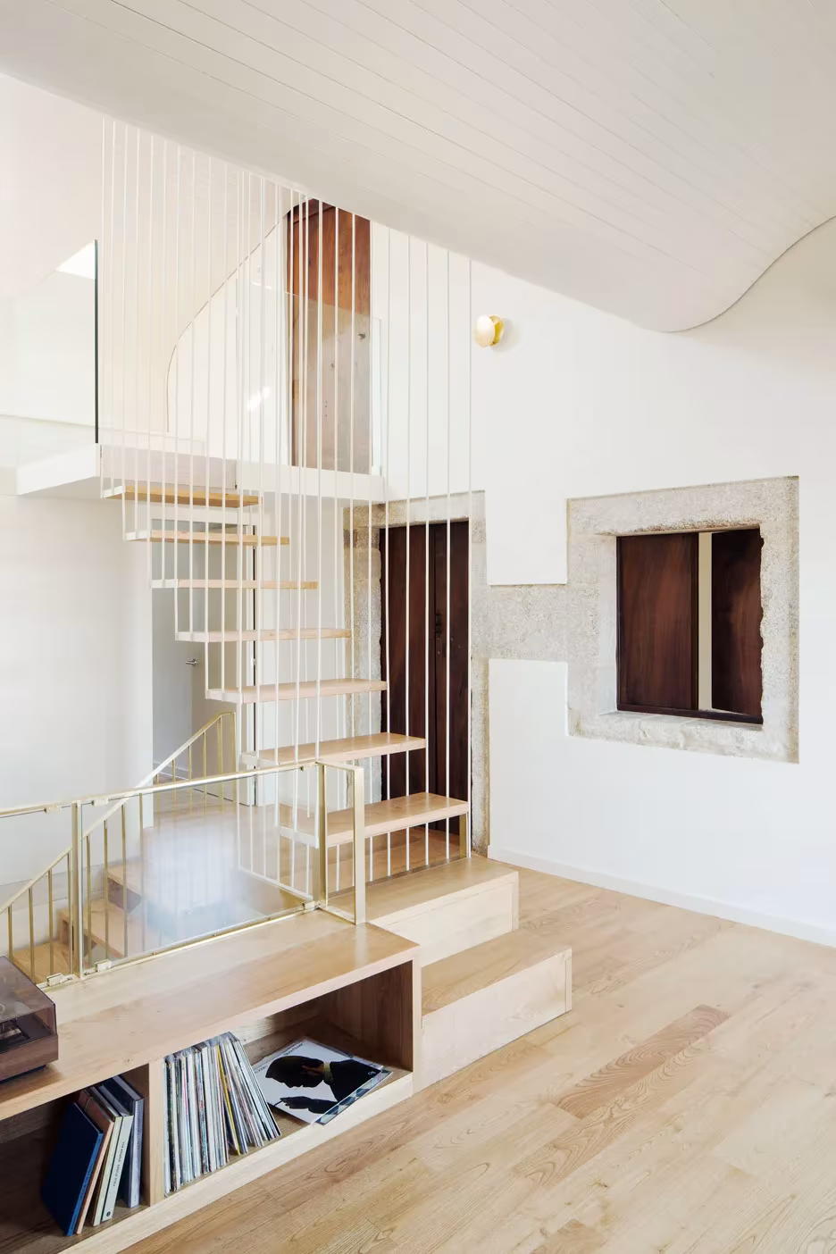 Escalera blanca ligera bajo techo ondulado en la Casa do Medio, con estantería de madera y discos