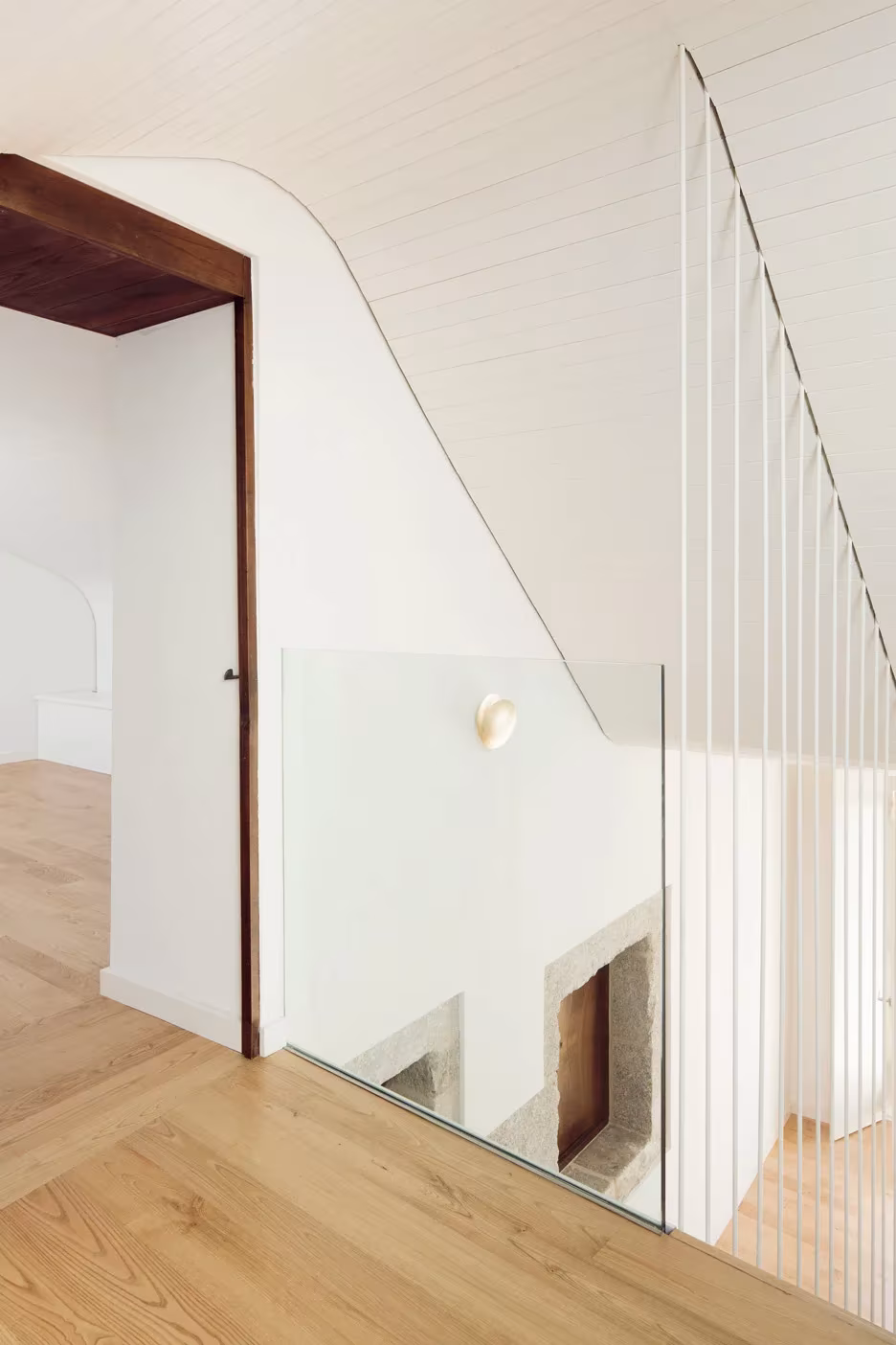 Rellano de la Casa do Medio con barandilla de varillas blancas, suelo de madera y puerta de marco oscuro