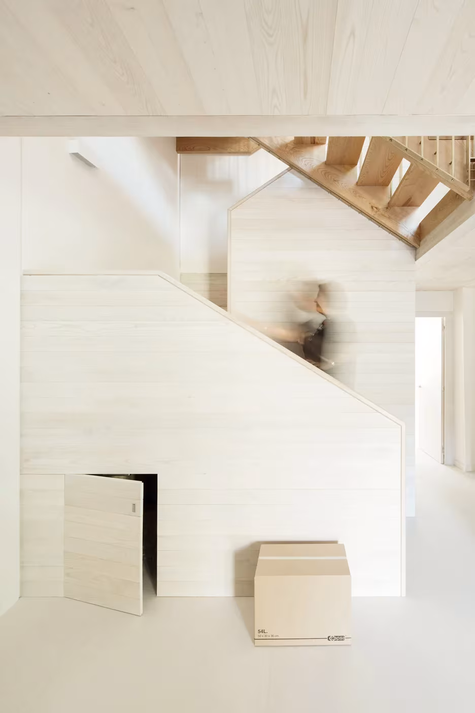 Volumen blanco bajo la escalera de la Casa do Medio con pequeña puerta y caja de madera en el suelo