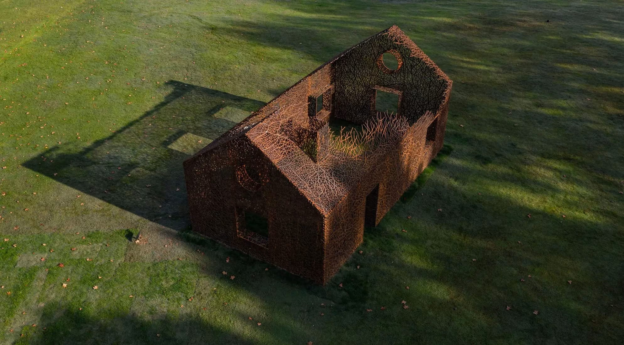 The Vanished House, silueta de casa en acero corten calado sobre una pradera, vista desde lo alto