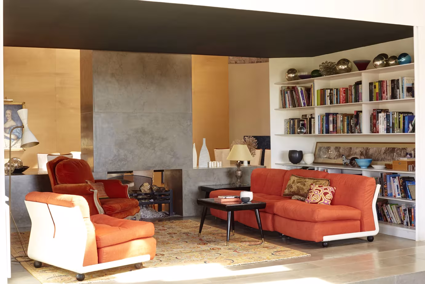 Salón de Wall Farm con sofás naranjas, chimenea exenta de hormigón y librerías blancas