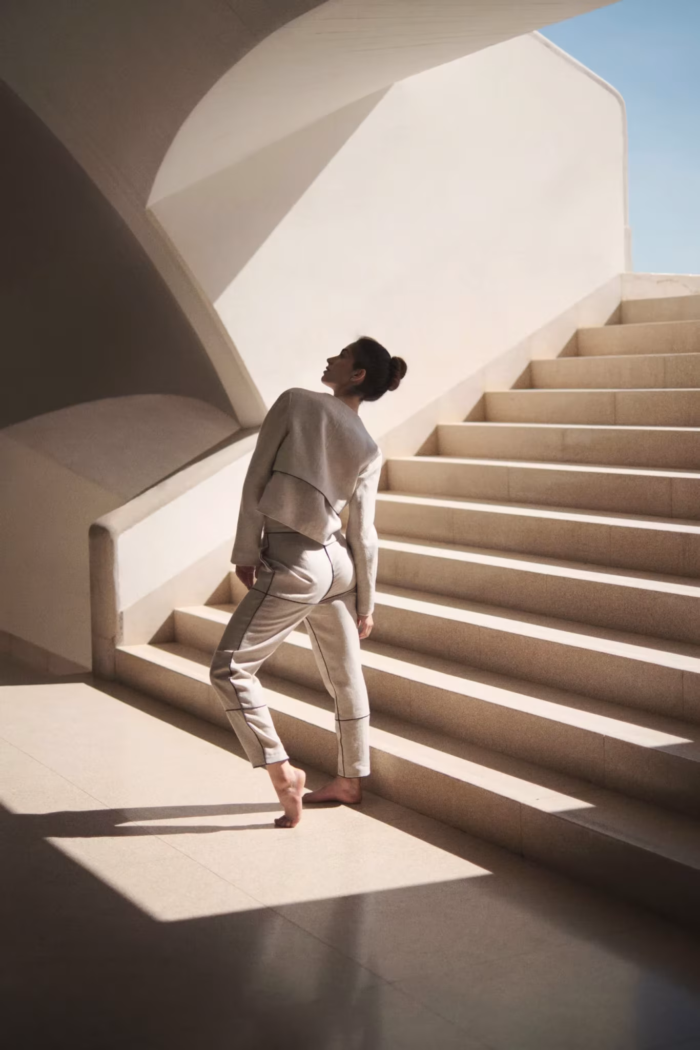 Bailarín de blanco junto a una escalera clara bañada por el sol bajo una bóveda curva