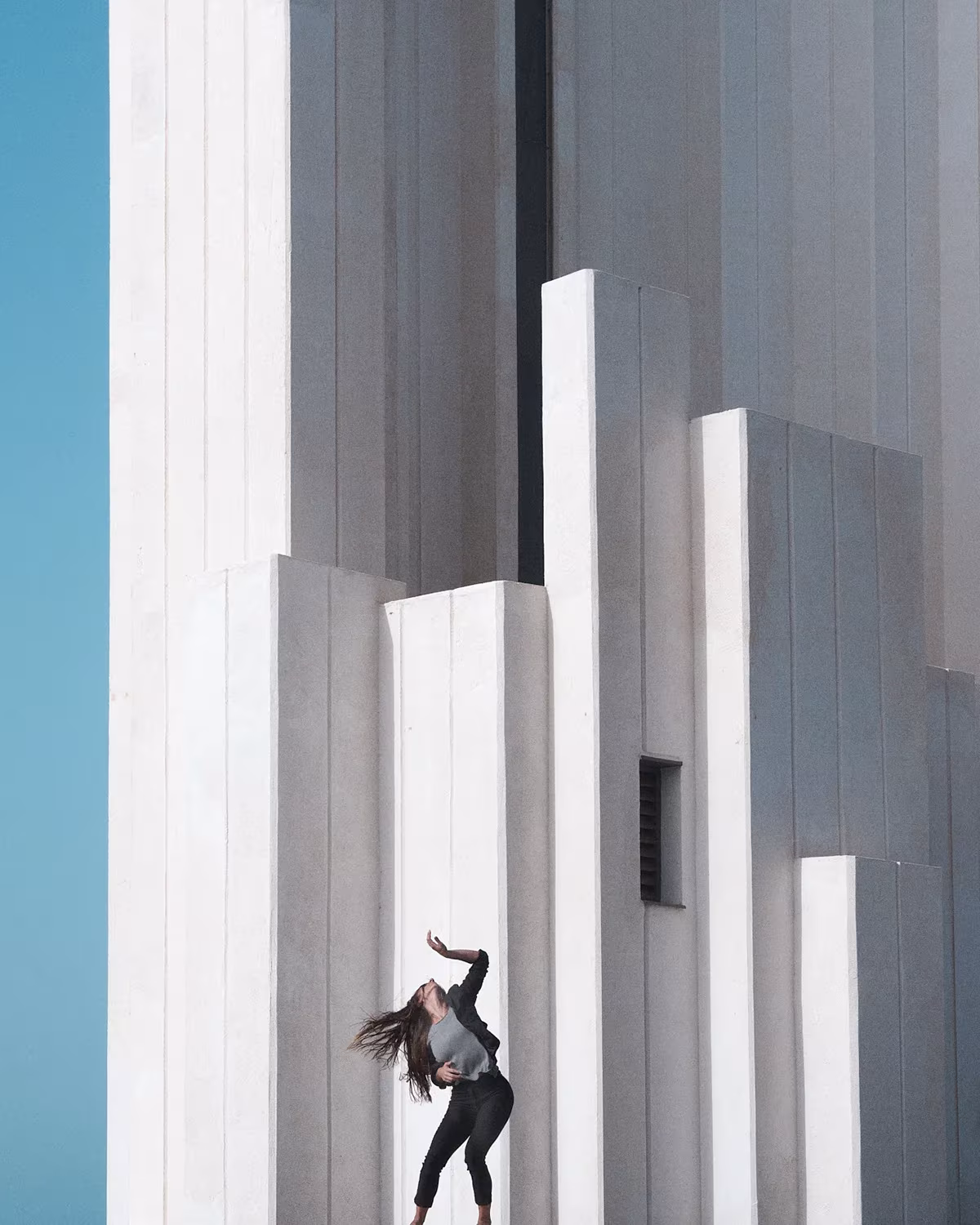 Bailarina arqueando el cuerpo ante una fachada de pilastras blancas escalonadas y cielo azul