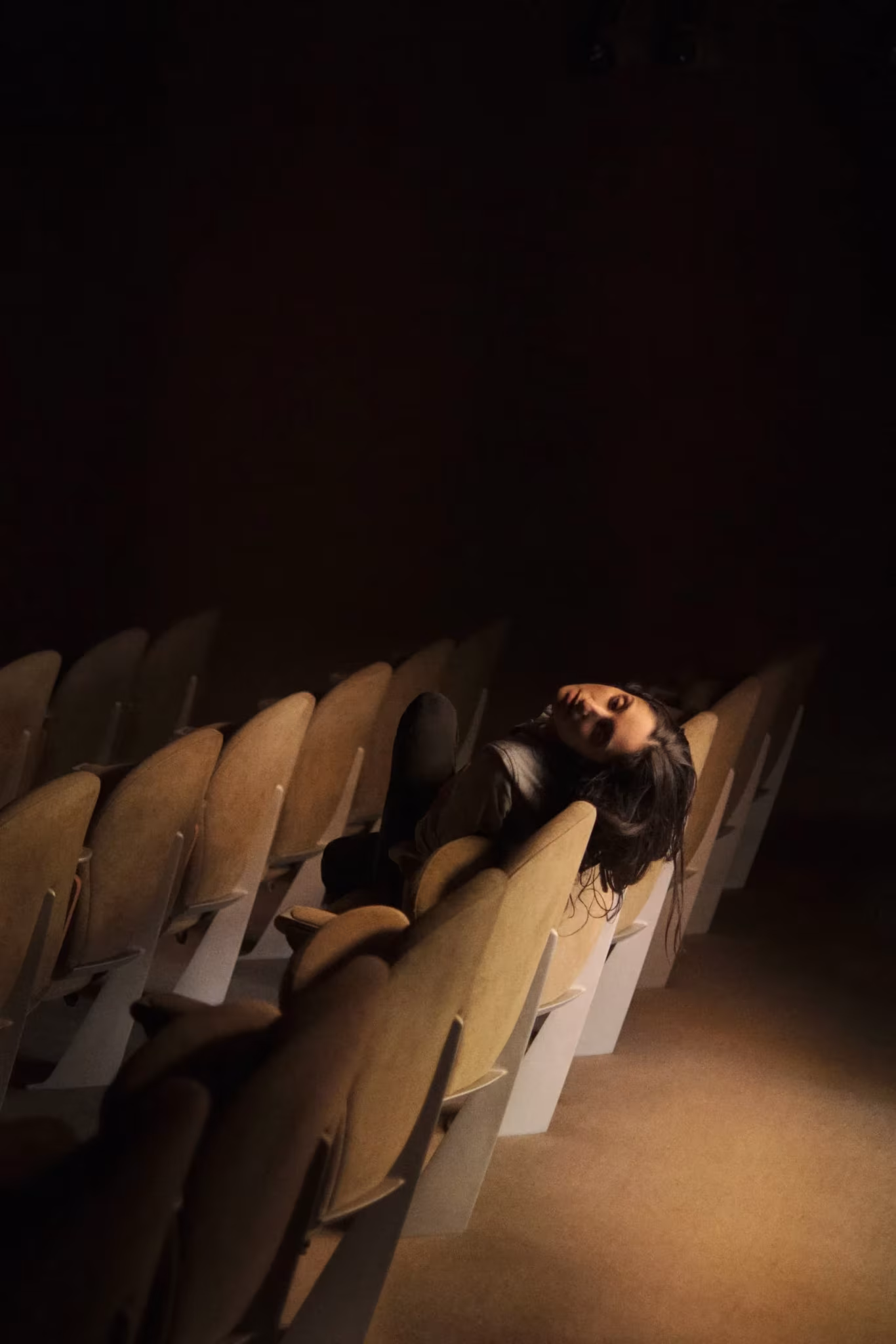 Persona recostada entre butacas de un auditorio en penumbra iluminada por un haz de luz