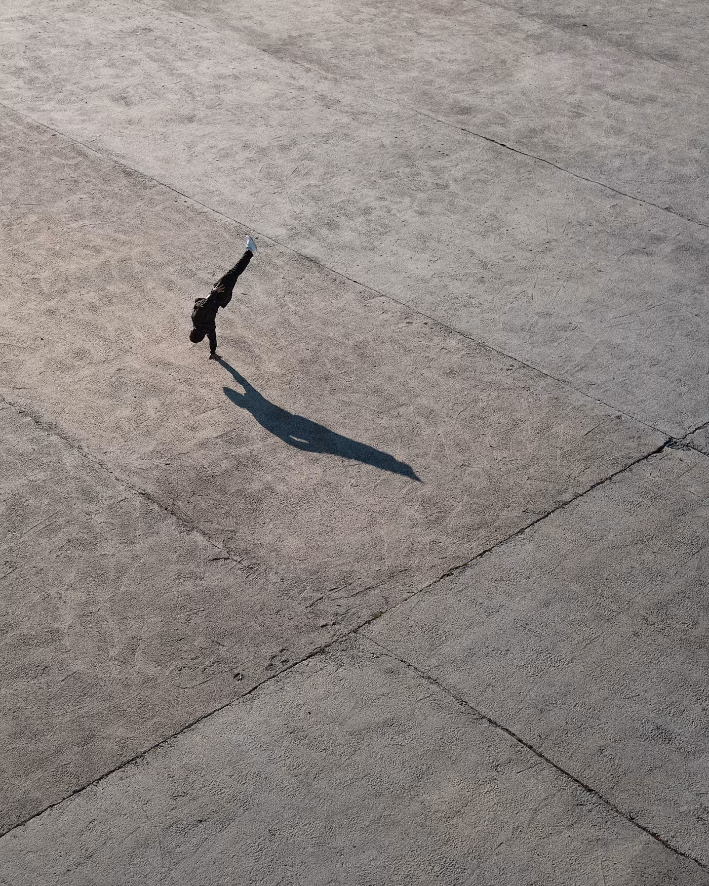 Vista cenital de un bailarín con larga sombra sobre una gran explanada de piedra gris
