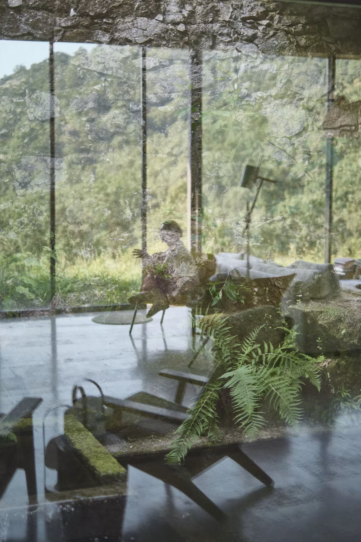 Interior acristalado con helechos, sillas cubiertas de musgo y reflejos de un bosque en el vidrio