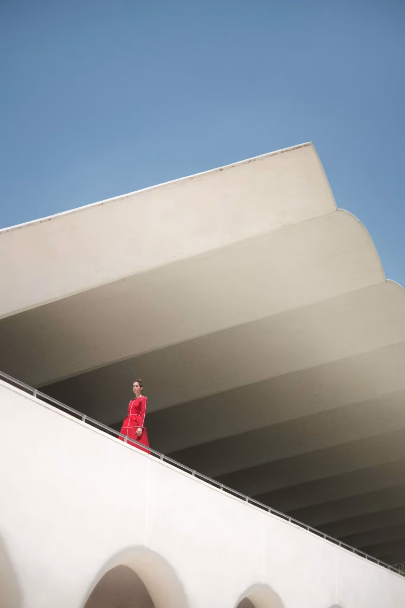 Figura de rojo bajando una rampa blanca bajo grandes voladizos escalonados contra el cielo