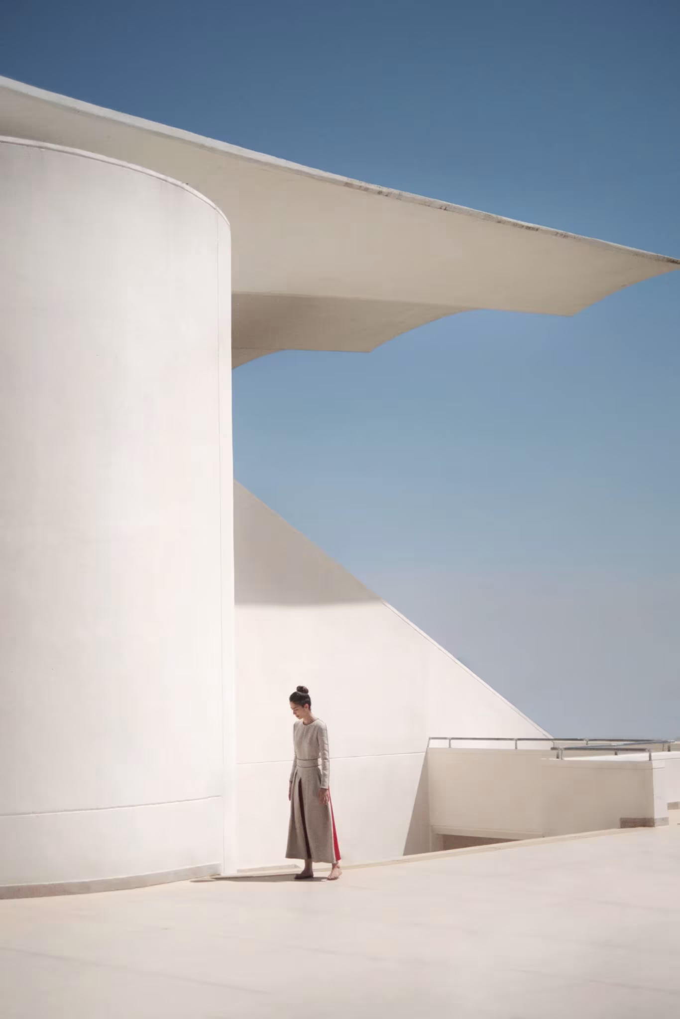 Mujer con vestido largo junto a un cilindro blanco bajo una cubierta volada y cielo azul