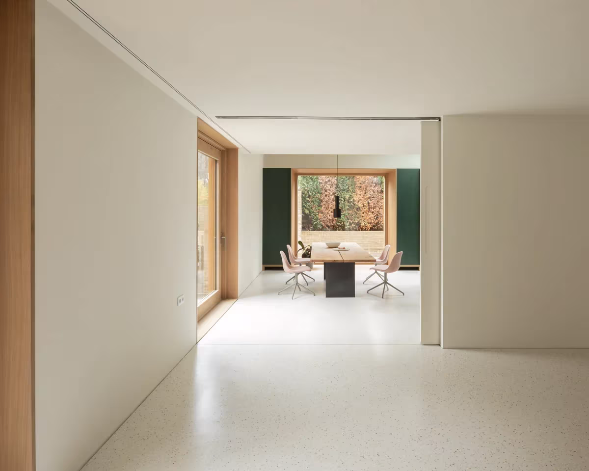Estancia diáfana de Fohlenweg con suelo continuo claro y ventana de marco de madera hacia el bosque