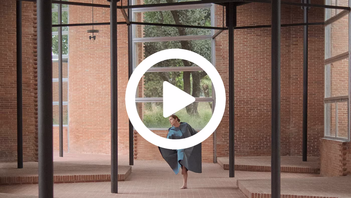 Fotograma de vídeo con una bailarina en un pabellón de ladrillo y estructura metálica, obra de Derek Pedros