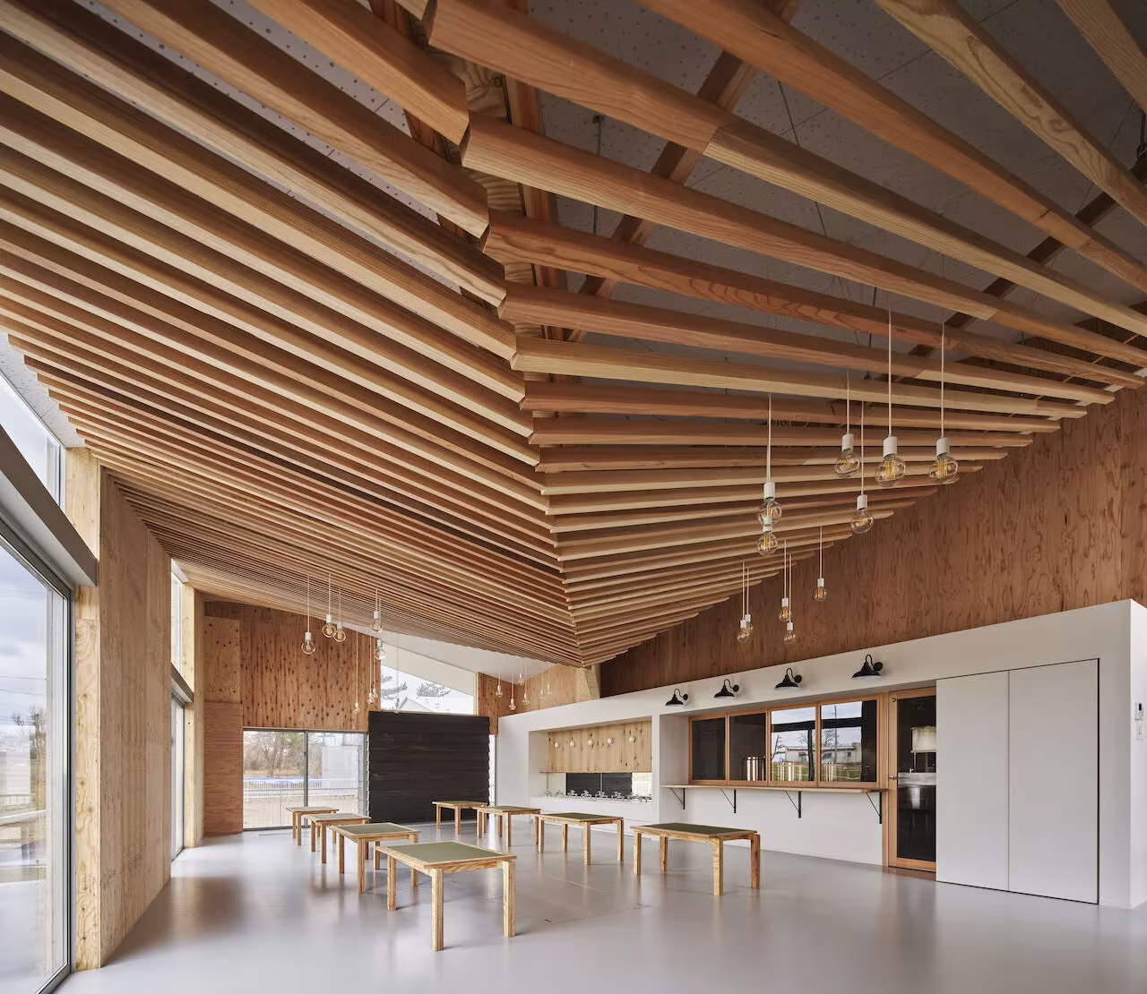 Comedor de la Escuela Infantil Yamaikarashi con mesas bajas de madera bajo un techo de listones inclinados