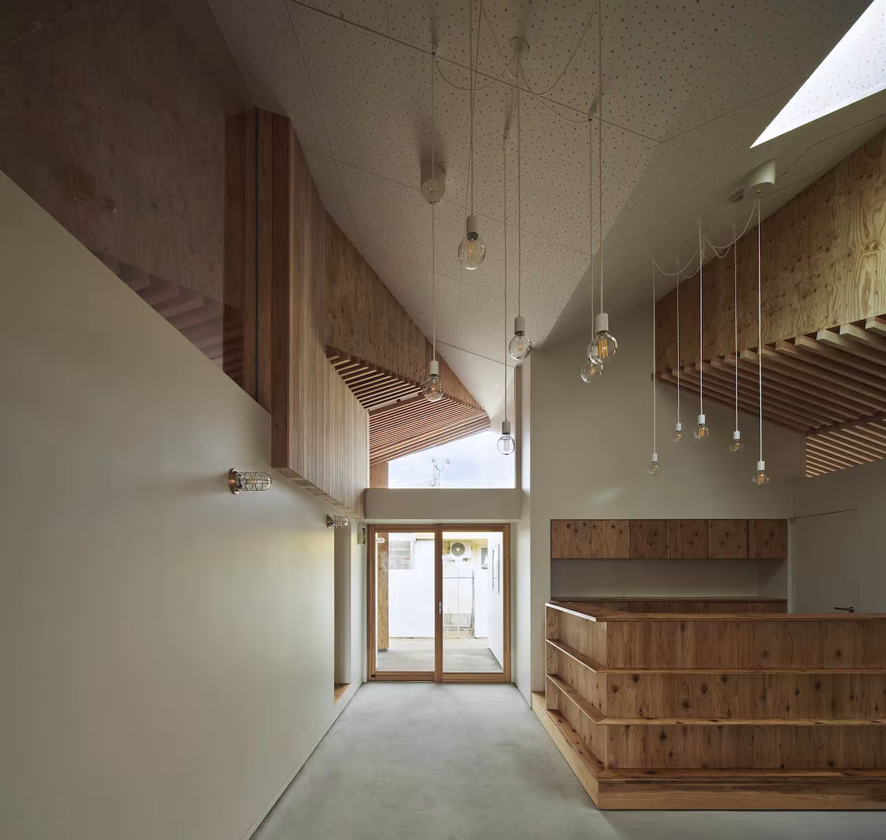 Vestíbulo de madera de la Escuela Infantil Yamaikarashi con mostrador de tablas y lucernario sobre la entrada