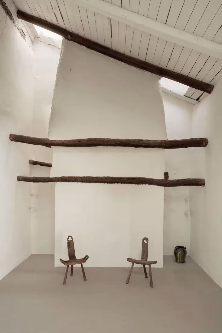 Sala encalada de gran altura con troncos de madera y dos sillas de tres patas en la Casa de la Sevillana
