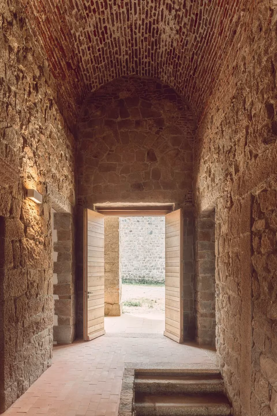 Galería abovedada de ladrillo y piedra con puerta de madera abierta al exterior en el Convento Saint-François